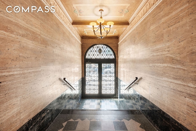 entryway with granite floors, wood walls, a chandelier, french doors, and crown molding