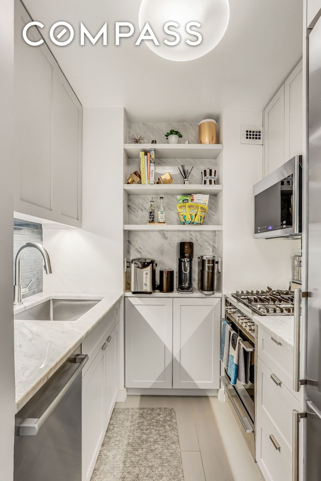 kitchen featuring stainless steel appliances, a sink, white cabinets, and light stone counters