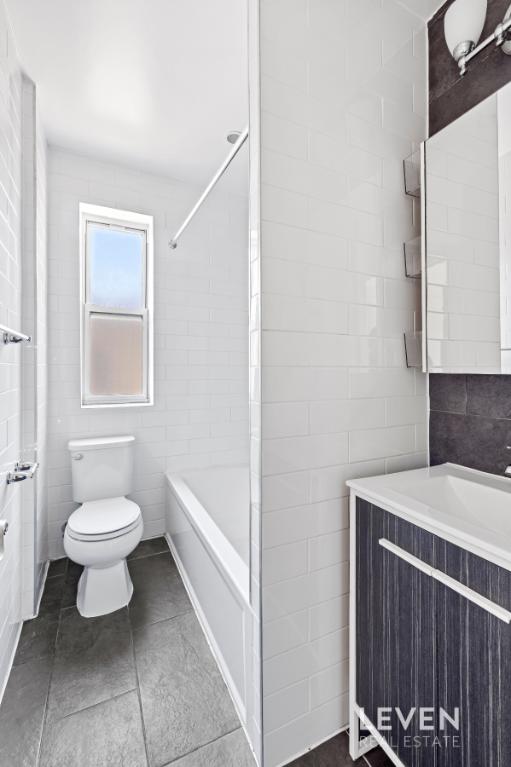 bathroom with toilet, vanity, tile patterned flooring, shower / washtub combination, and tile walls