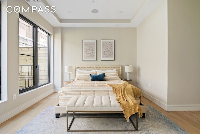 bedroom with light wood finished floors, a raised ceiling, and baseboards