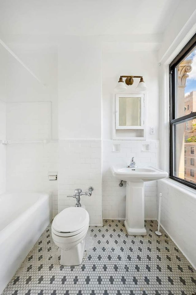 bathroom with toilet, tile patterned flooring, a wainscoted wall, tile walls, and a sink