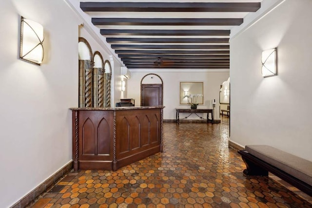 hall featuring beamed ceiling, a wall unit AC, dark stone finish flooring, and baseboards