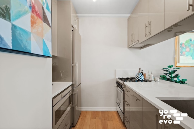 kitchen featuring premium appliances, light wood finished floors, light countertops, ornamental molding, and baseboards