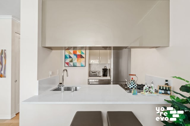 kitchen featuring a sink, a peninsula, wall chimney exhaust hood, light countertops, and modern cabinets