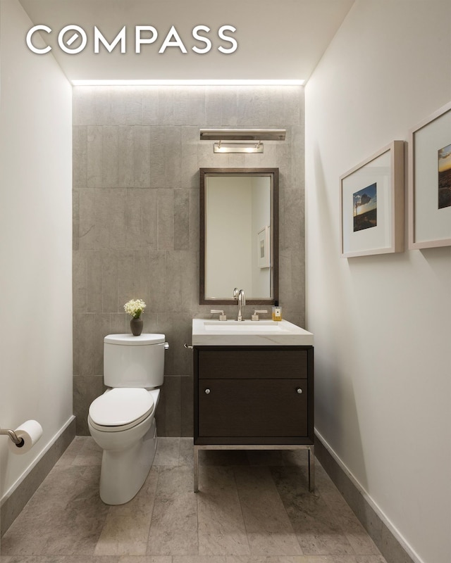 bathroom featuring toilet, vanity, baseboards, and tile walls