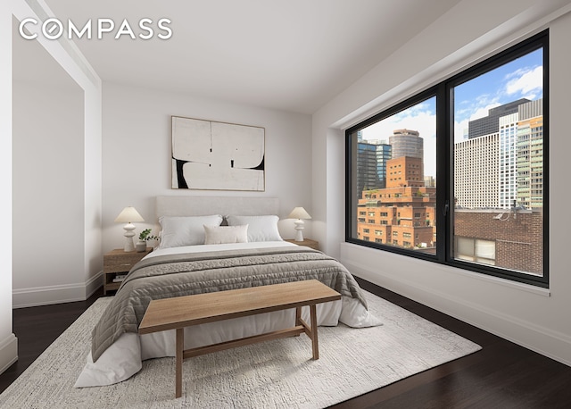 bedroom featuring dark wood finished floors, baseboards, and a city view
