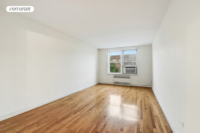 spare room featuring radiator heating unit, light wood-style floors, cooling unit, and baseboards