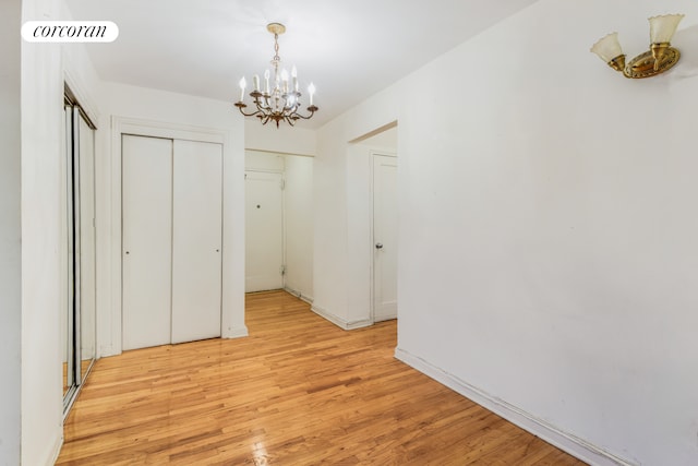 hall featuring a chandelier, light wood-type flooring, and baseboards
