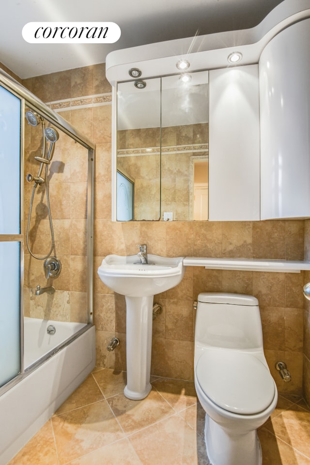 bathroom with tile walls, enclosed tub / shower combo, and toilet