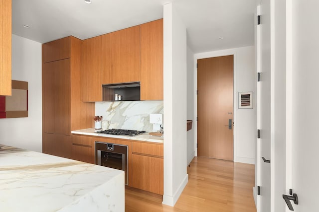 15 E 30th St Unit 21C, New York City, NY 10016 - kitchen featuring wine cooler, stainless steel gas cooktop, light wood-style flooring, decorative backsplash, and brown cabinets