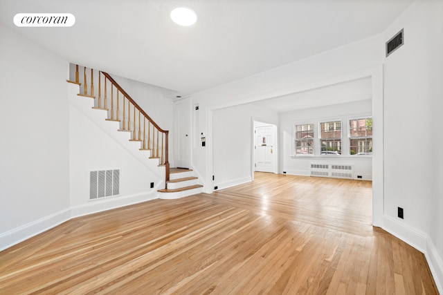 unfurnished living room featuring radiator heating unit, stairway, light wood-type flooring, and baseboards