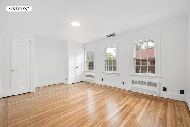 unfurnished bedroom with radiator, light wood finished floors, multiple closets, and baseboards