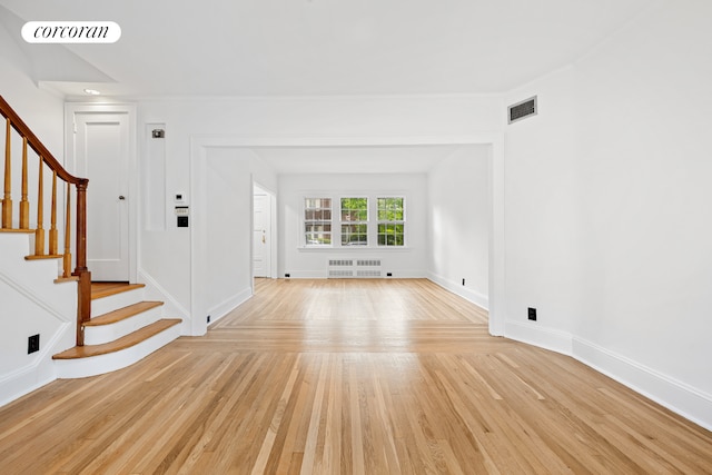 unfurnished living room with radiator, light wood-type flooring, stairs, and baseboards