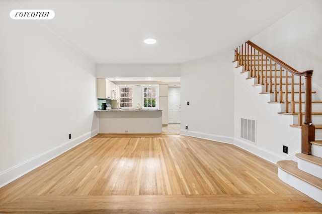 unfurnished living room with stairs, light wood-style floors, baseboards, and recessed lighting