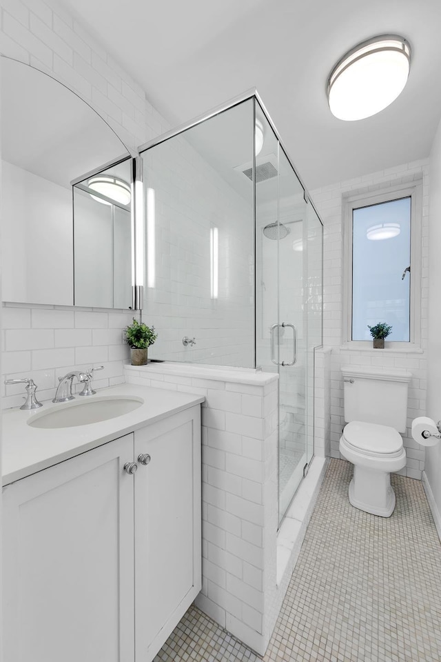 bathroom with tile walls, a shower stall, toilet, vanity, and tile patterned flooring