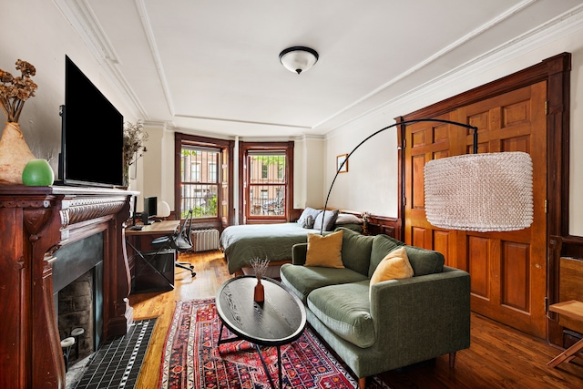 bedroom featuring a fireplace with flush hearth, radiator heating unit, wood finished floors, a raised ceiling, and ornamental molding