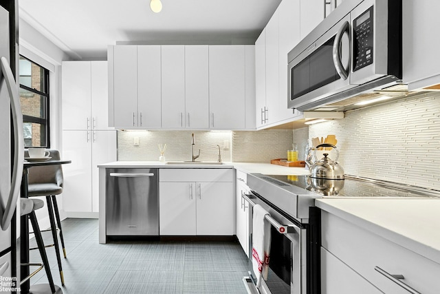 kitchen featuring appliances with stainless steel finishes, a sink, light countertops, white cabinets, and tasteful backsplash