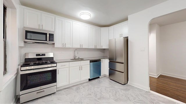 221 E 18th St Unit 1E, New York City, NY 11226 - kitchen with stainless steel appliances, a sink, white cabinets, arched walkways, and baseboards
