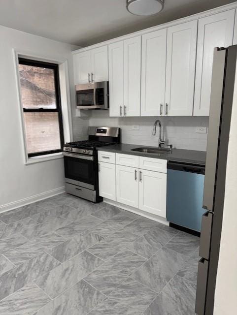 kitchen with stainless steel appliances, a sink, dark countertops, and baseboards