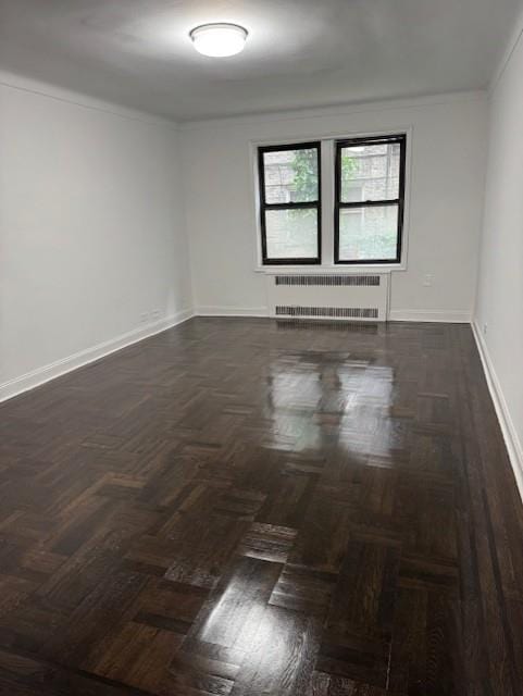 empty room featuring radiator heating unit, baseboards, and crown molding