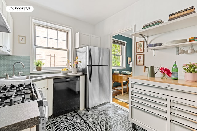kitchen featuring appliances with stainless steel finishes, a sink, white cabinets, open shelves, and decorative backsplash