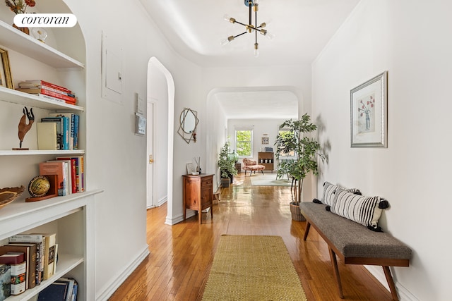 corridor with arched walkways, light wood finished floors, and baseboards