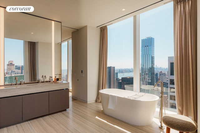 bathroom with a city view, expansive windows, wood finished floors, a soaking tub, and vanity