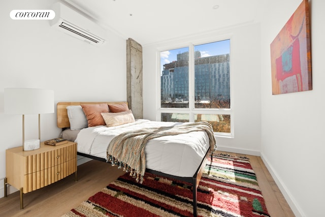 bedroom featuring a wall mounted AC, wood finished floors, and baseboards
