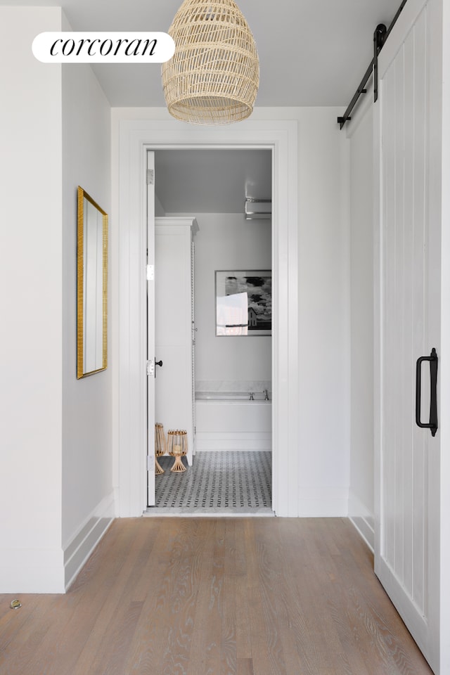 hallway featuring a barn door, wood finished floors, and baseboards