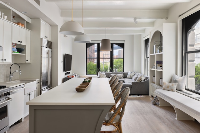 kitchen featuring high end fridge, a kitchen island, light countertops, beamed ceiling, and light wood-type flooring