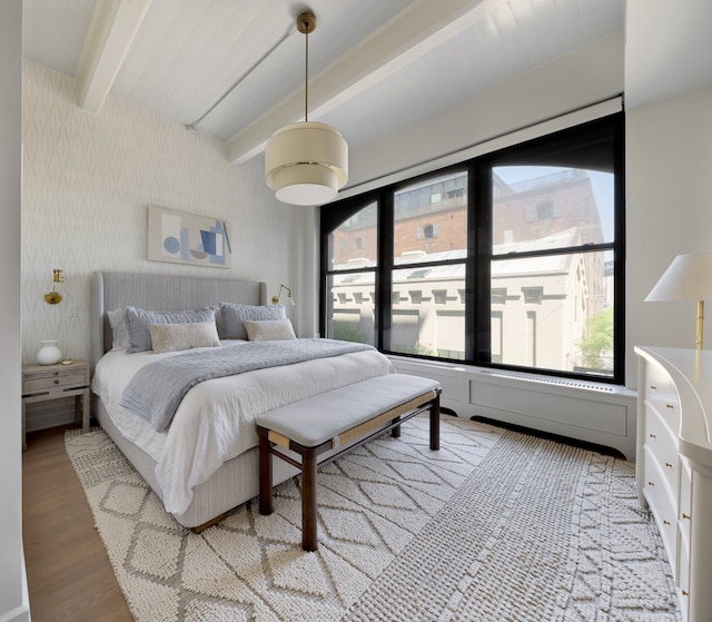 bedroom featuring beam ceiling, wallpapered walls, multiple windows, and light wood-style floors