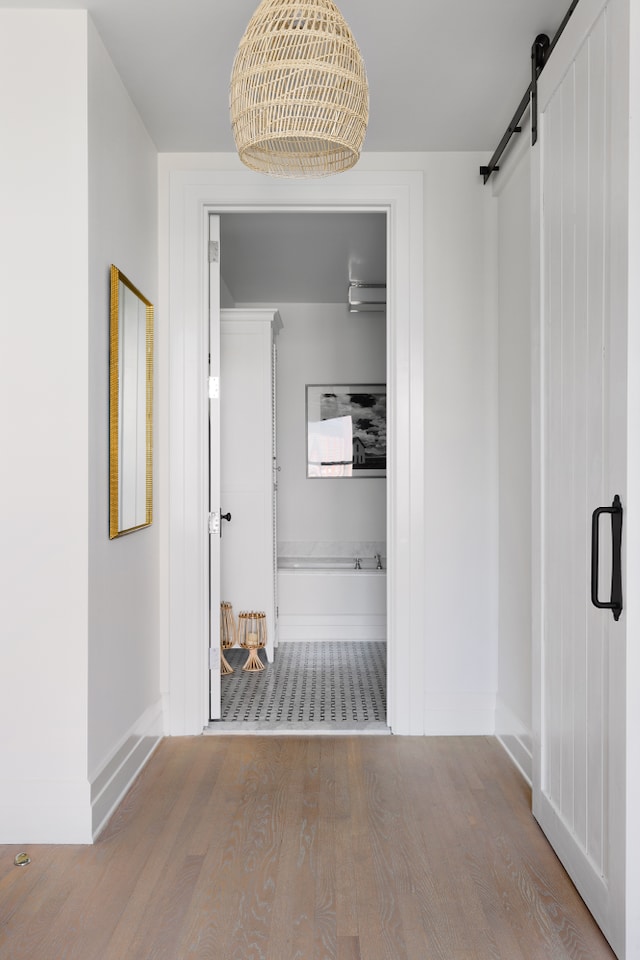 corridor featuring a barn door, wood finished floors, and baseboards
