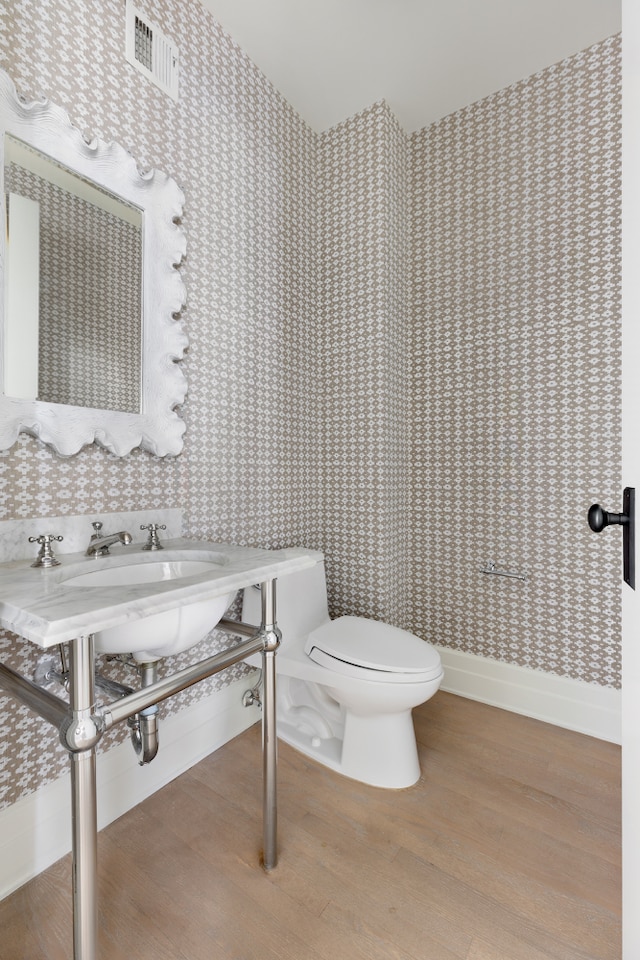 bathroom with wood finished floors, toilet, baseboards, and wallpapered walls