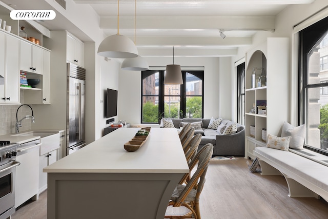kitchen with appliances with stainless steel finishes, a center island, beamed ceiling, light countertops, and light wood finished floors