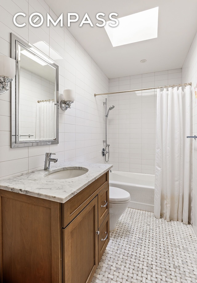 full bathroom with tile walls, a skylight, vanity, toilet, and shower / bath combo
