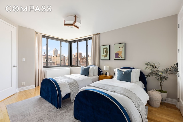 bedroom featuring light wood-style flooring, a skyline view, and baseboards