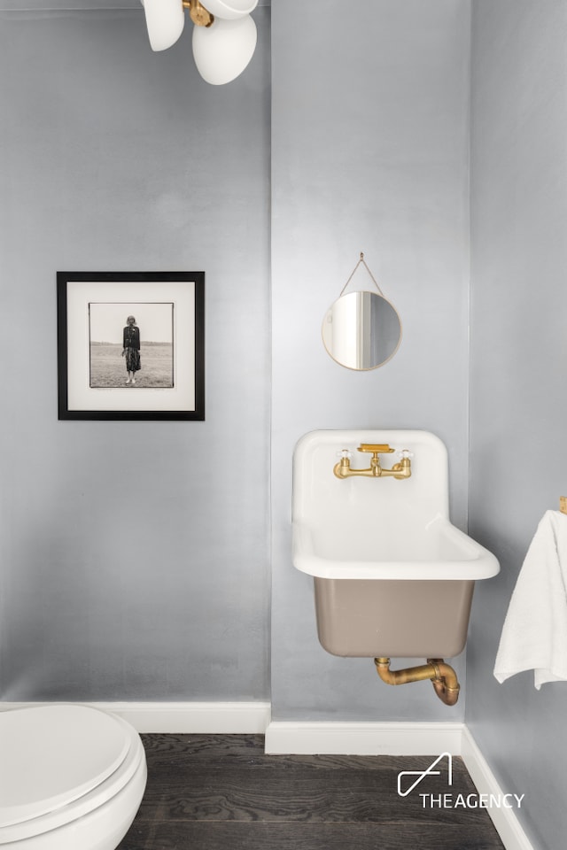 bathroom featuring baseboards, wood finished floors, toilet, and a sink