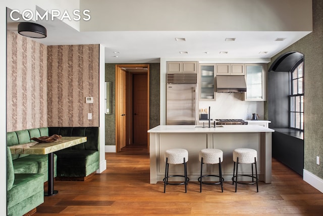 kitchen featuring built in fridge, under cabinet range hood, a sink, and light wood finished floors