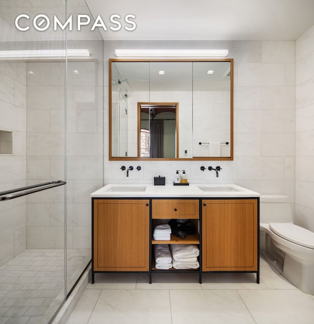 bathroom with a shower stall, tile walls, toilet, and double vanity