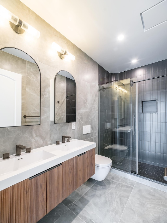 bathroom with tile walls, toilet, a stall shower, marble finish floors, and double vanity