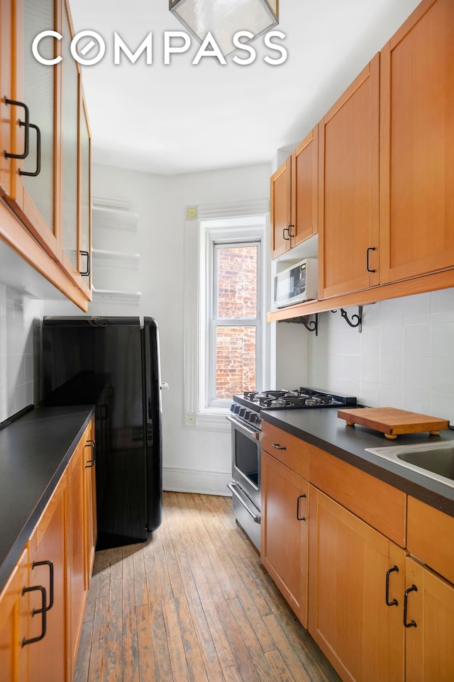 306 W 4th St Unit D3, New York City, NY 10014 - kitchen featuring dark countertops, stainless steel range with gas stovetop, tasteful backsplash, light wood-type flooring, and baseboards