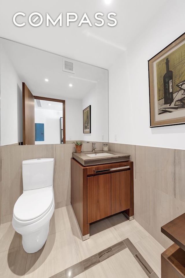 bathroom featuring tile walls, a wainscoted wall, toilet, and vanity