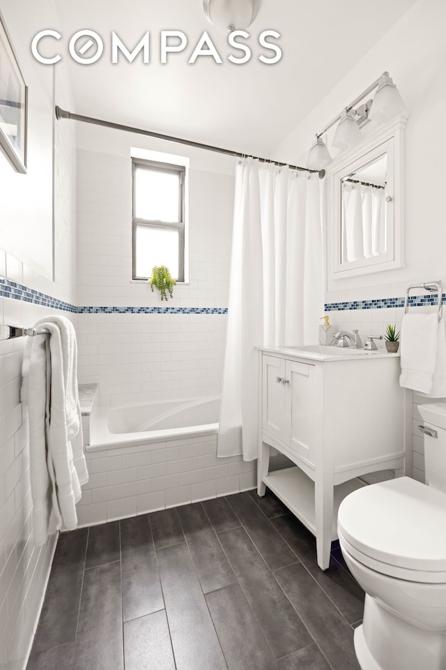 full bathroom featuring toilet, tiled shower / bath combo, vanity, and tile walls