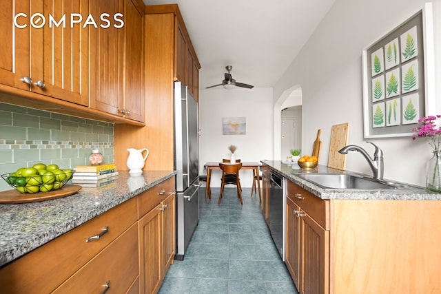kitchen featuring a sink, stainless steel appliances, brown cabinets, decorative backsplash, and ceiling fan