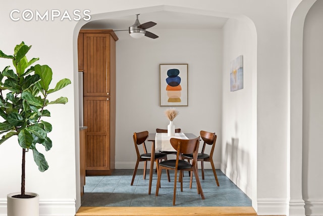 tiled dining room with arched walkways, a ceiling fan, and baseboards
