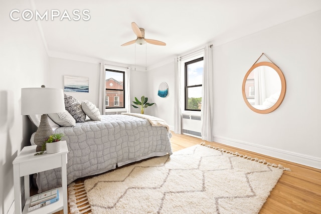 bedroom with light wood-type flooring, crown molding, baseboards, ceiling fan, and radiator