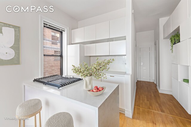 kitchen featuring light wood-style flooring, white cabinetry, light countertops, a breakfast bar area, and modern cabinets