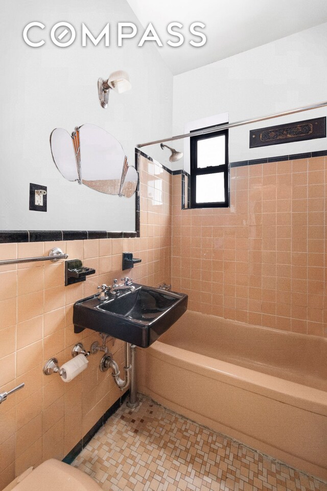 full bathroom featuring tile walls, shower / bath combination, a sink, and a wainscoted wall