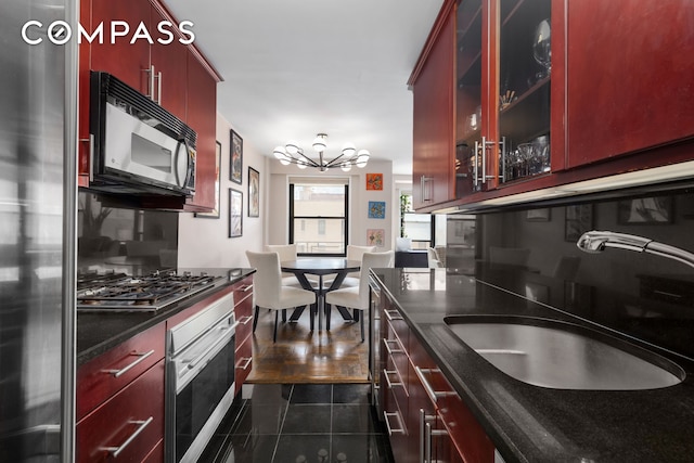 kitchen with stainless steel appliances, a sink, dark tile patterned flooring, a chandelier, and dark brown cabinets