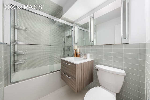 bathroom with tile walls, toilet, shower / bath combination with glass door, vanity, and tasteful backsplash
